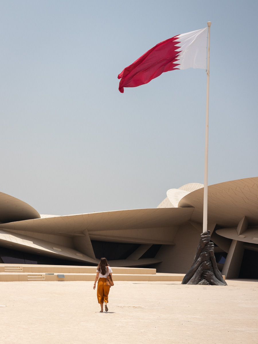 A woman walking beneath the Qatari flag at the National Museum in Doha